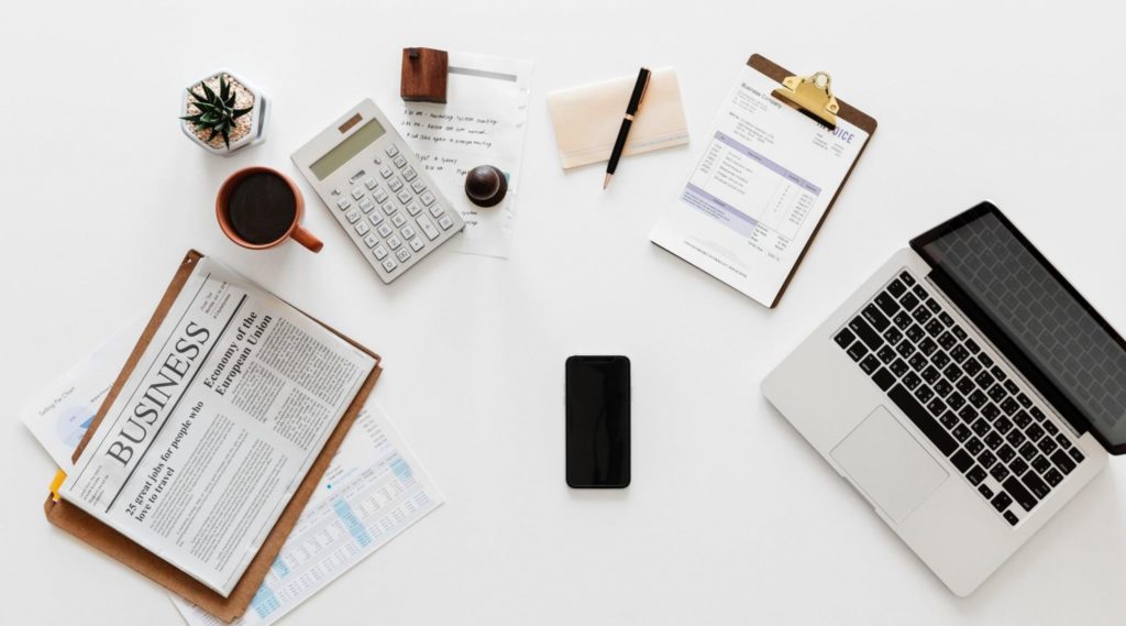 workspace with a laptop, smartphone, calculator, coffee cup, financial documents