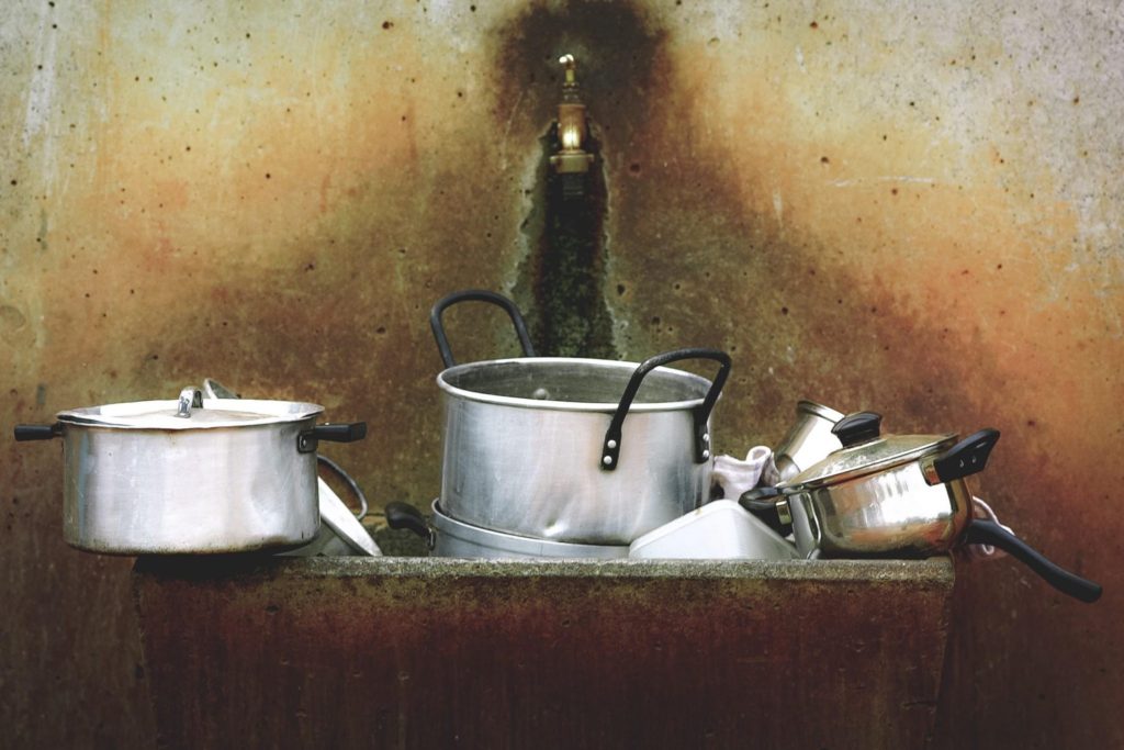 Used cooking pots and pans piled in a stained kitchen sink
